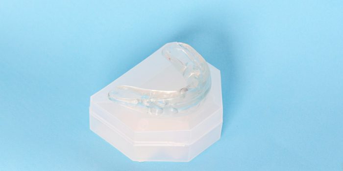 Silicone dental mouthguard, orthodontic trainer to correct bite on blue background